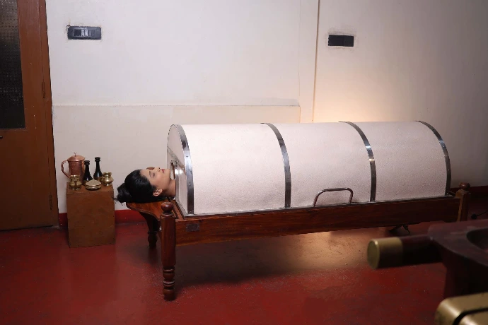 Patient receiving Swedana steam therapy in the wooden steam chamber at Tapasya Health & Wellness