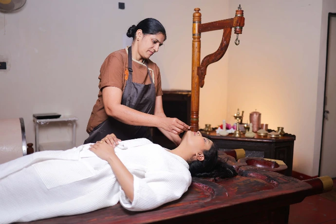 Therapist performing Shirodhara head therapy on a droni table at Tapasya Health & Wellness